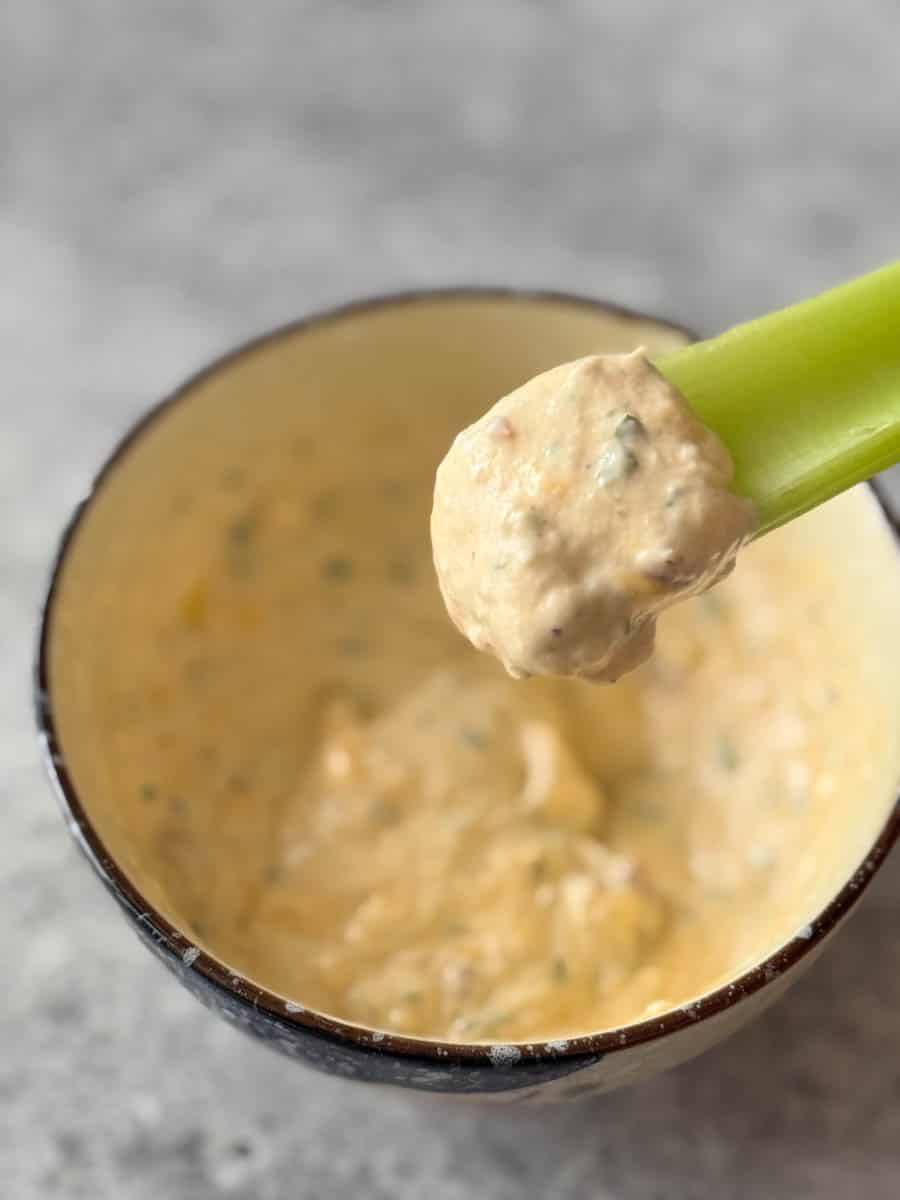 dipping celery stick into the white chicken bacon dip