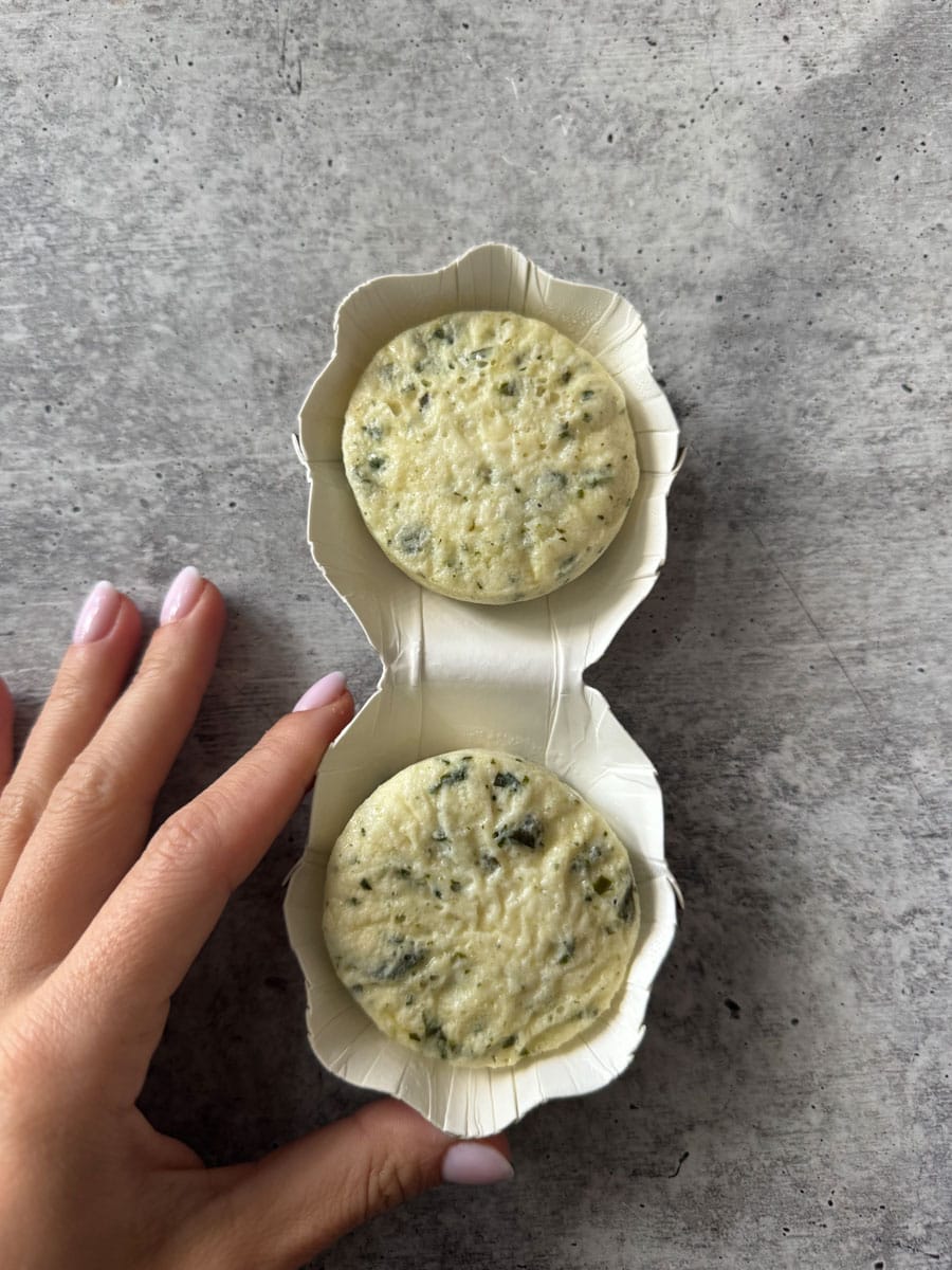 Spinach and cheese muffins in a paper container, held by a hand on a gray surface. Perfect for a hea.