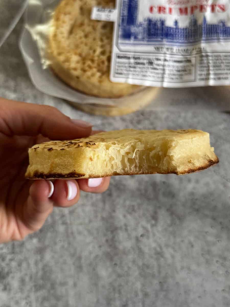 Hand holding a slice of fresh bread with a bread bag in the background.