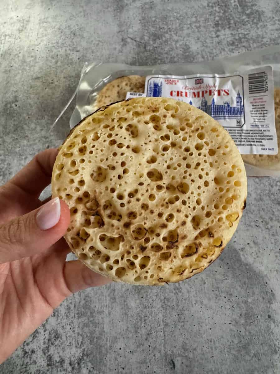 Close-up of a fresh, toasted English muffin held in hand with packaging in background.