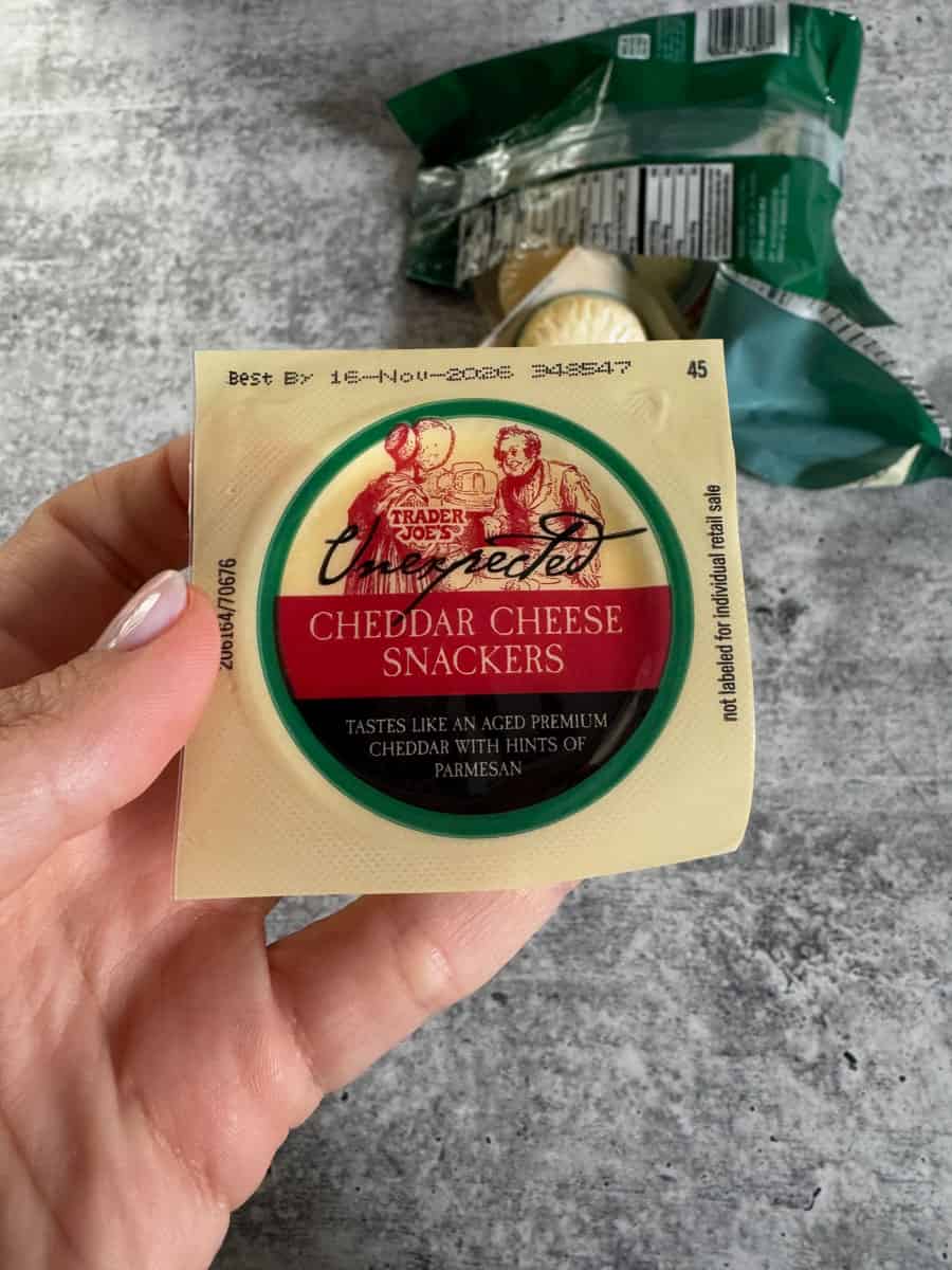Trader Eats cheddar cheese snackers in hand with snack bag in background.