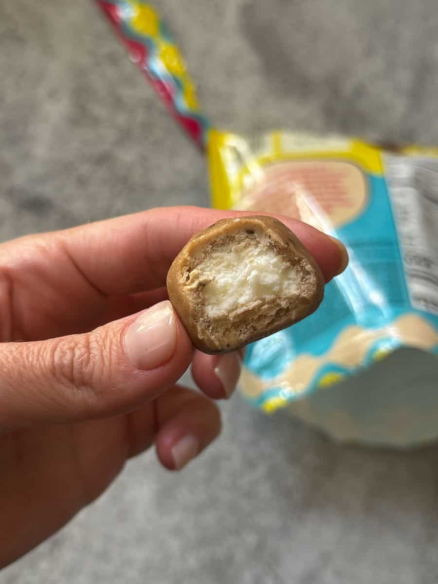 Close-up of a hand holding a bitten mini biscuit with a snack package in the background.