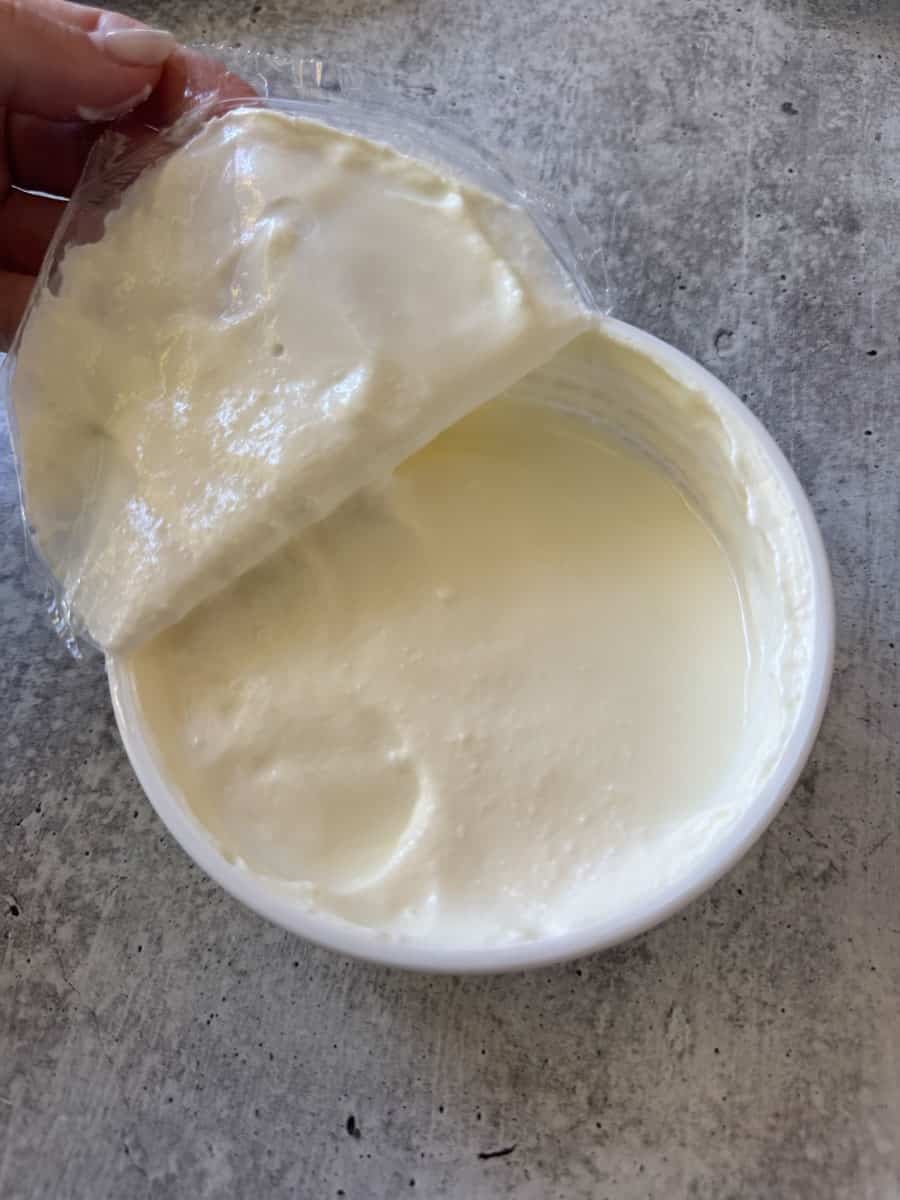 Cream cheese spread with a partially peeled plastic cover, creamy and smooth texture, on a gray surf.