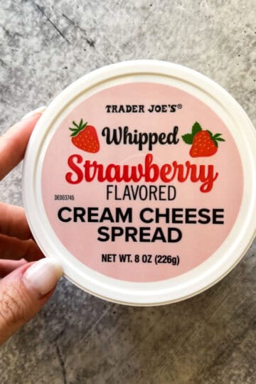 Trader Joe's strawberry flavored cream cheese spread in a round container, hand holding it.